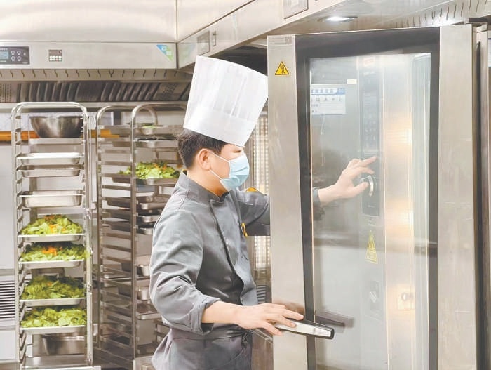 廚師在後廚操作蒸烤機器人,加工製作食堂飯菜。 廚師在後廚操作蒸烤機器人,加工製作食堂飯菜。