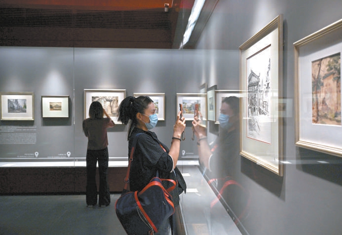 游客仔细观赏展品，记录澳门历史建筑的细节。