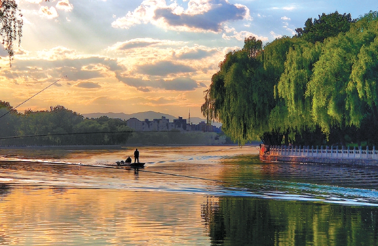 黄昏时分，在京城什刹海，站在银锭桥西望，碧波倒映着绿柳、霞光，归航的作业扁舟点缀其间，远处的群山依稀掩映，构成一幅诗情画意的宁静画卷。