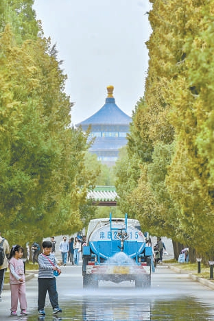 3月23日中午，天坛公园东门内，工作人员对树木密集的路面进行洒水作业。