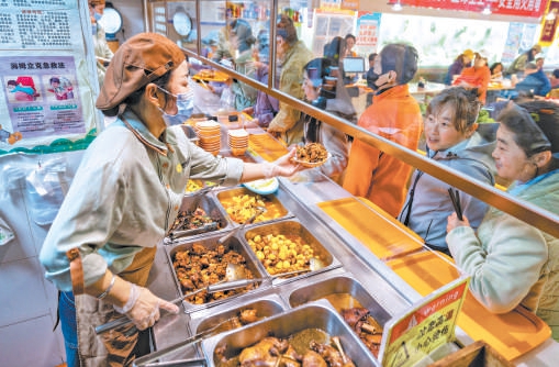 美意延年综合服务中心内的社区食堂，餐台菜品丰富，居民排队取餐。