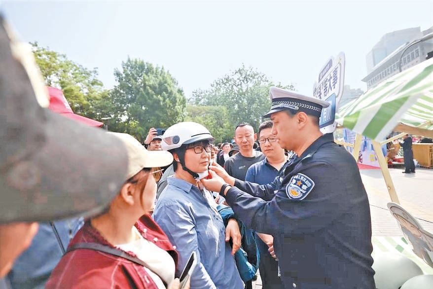活动现场，交警向市民演示安全头盔的佩戴方式。