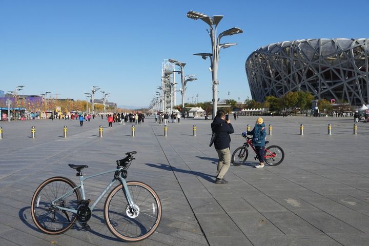 在北京奧林匹克公園，一位家長帶着孩子騎行參觀“鳥巢”（11月17日攝）。