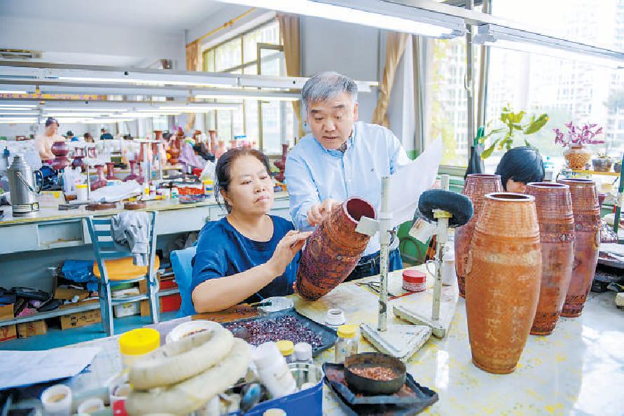 林徽因第二代弟子、景泰藍非遺傳人鐘連盛（右）與學生、員工們一起研究景泰藍製作。 （潘之望 攝）