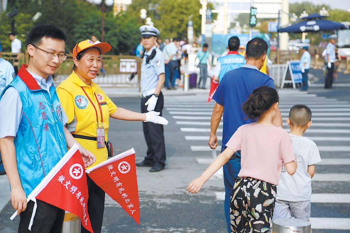 在長安街臺基廠路口，交通文明引導員和青年志願者一起，引導行人文明過馬路，協助維護路口交通秩序。