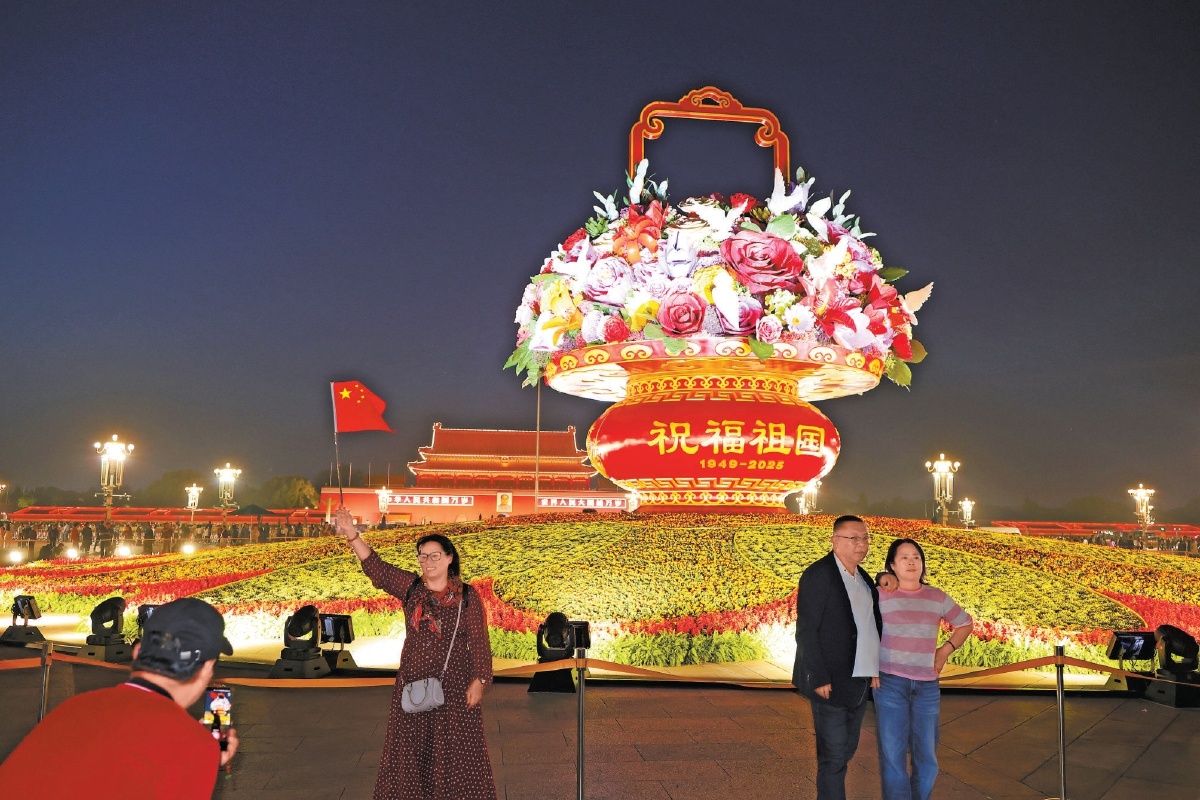 天安門廣場“祝福祖國”巨型花籃燈光璀璨，游客在夜色中與花籃合影。