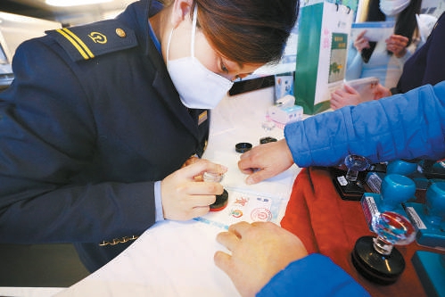 京张高铁上设置的流动邮局备受旅客青睐，“雪之梦”乘务组乘务员会为游客在纪念册上盖上纪念图章。