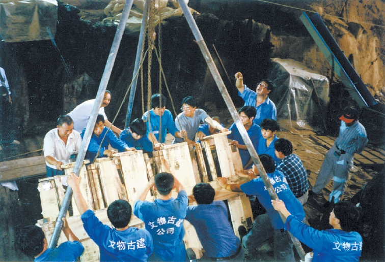 考古队员用木板把大漆案固定住，用吊车吊出来。