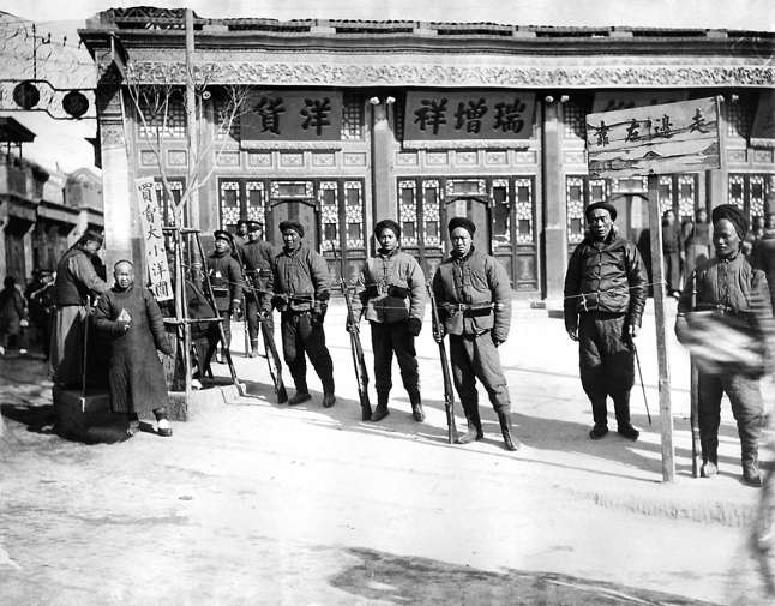 这张1909年拍摄的照片中，左边胡同的门头虽然没有被完整地拍摄下来，但仅凭露出的两个字就能猜到这是位于前门大街东侧的打磨厂，与西河沿东西相对。门头上共五个字，其中“打磨厂”三字居中较高，“西口”两字则略低分居两端。胡同口南侧是著名的“瑞增祥”绸布店。