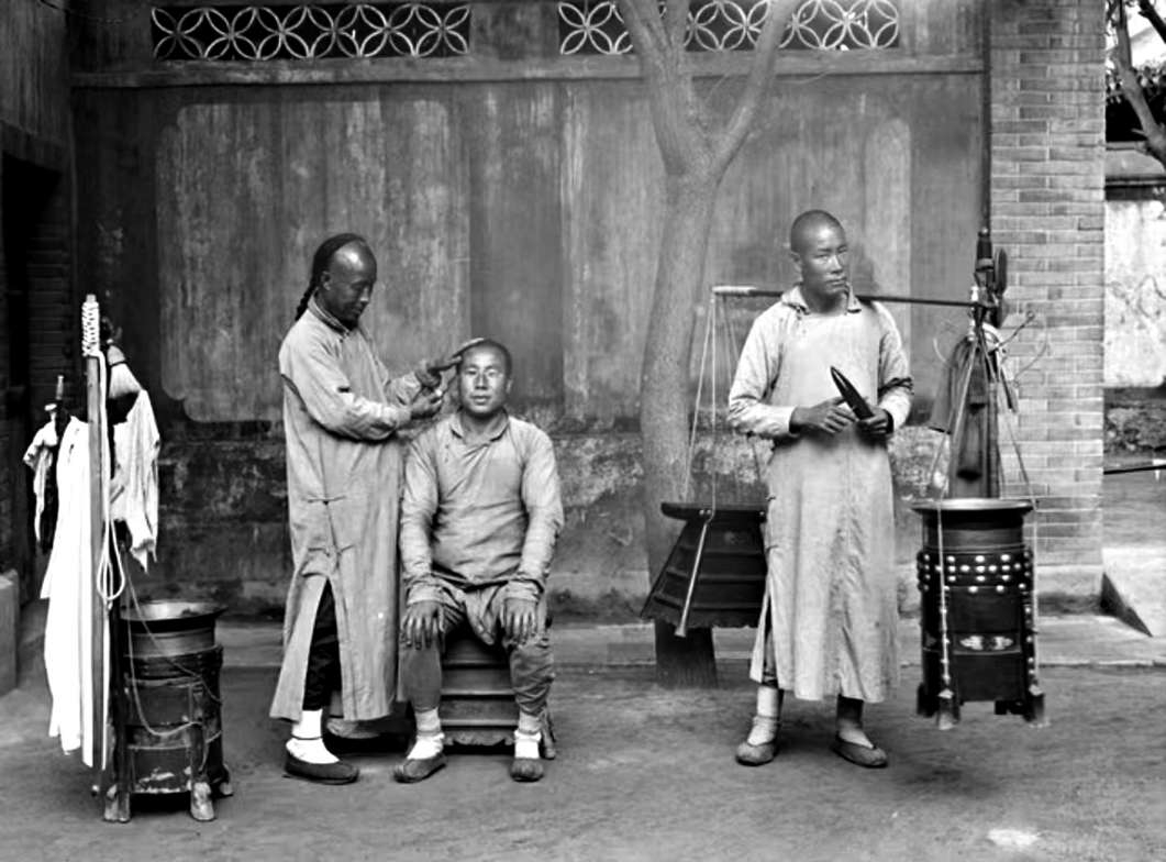 1905年，北京街头的剃头挑子。一头是板凳与工具箱，一头是烧热水洗头用的火炉。至今北京有句俏皮话：剃头挑子一头热，说的就是这个。