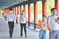2021年8月10日，在天坛公园长廊，工作人员手举“戴口罩不聚集”提示牌巡视，提醒游客做好防护。（邓伟 摄）