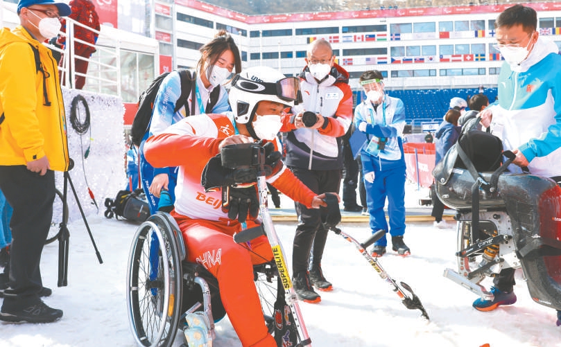 在2022年3月10日进行的残奥高山滑雪男子大回转决赛现场，志愿者贴心地为完赛的选手推来轮椅，方便运动员休整。（武亦彬 摄）