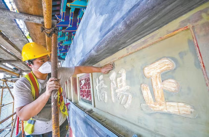 昨天，在前门五牌楼施工现场，工人正在细心进行翻新工作。五牌楼正中牌匾上的“正阳桥”三字将重新贴金。