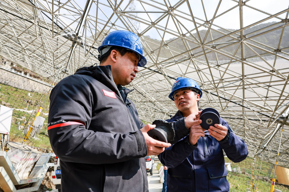 2023年2月13日，姜鹏（左）在贵州“中国天眼”的反射面板下与工作人员交谈（维护保养期间拍摄）。