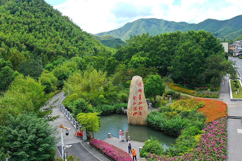 在浙江省湖州市安吉县余村，游客在刻有“绿水青山就是金山银山”的石碑前留影（2025年8月6日摄，无人机照片）。