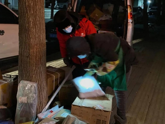 光明街道东兴二区志愿者寒夜协助快递员投寄快递。