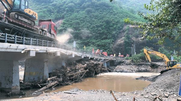 青白口桥主体结构局部下陷，抢险人员正在桥旁加急建设临时跨河通路。