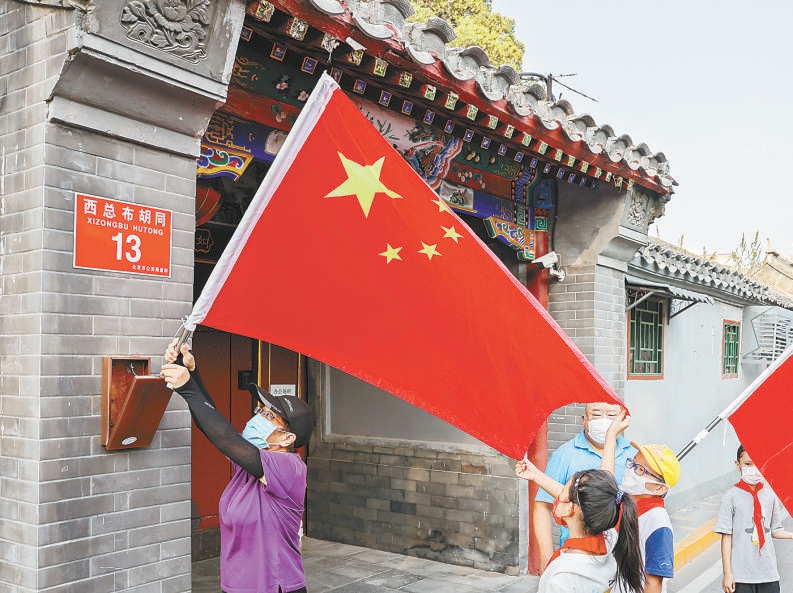 在东城区建国门街道西总布胡同，居民与小学生一起挂国旗迎国庆。