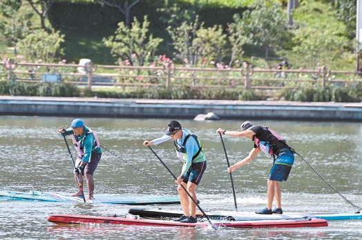 桨板邀请赛选手躬身挥桨，在千年运河之上迎风竞逐。
